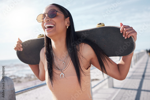 Happy, summer and woman by ocean with skateboard for weekend, holiday and vacation in trendy style. Fashion, laughing and person skateboarding for activity, freedom and adventure by broadwalk seaside photo