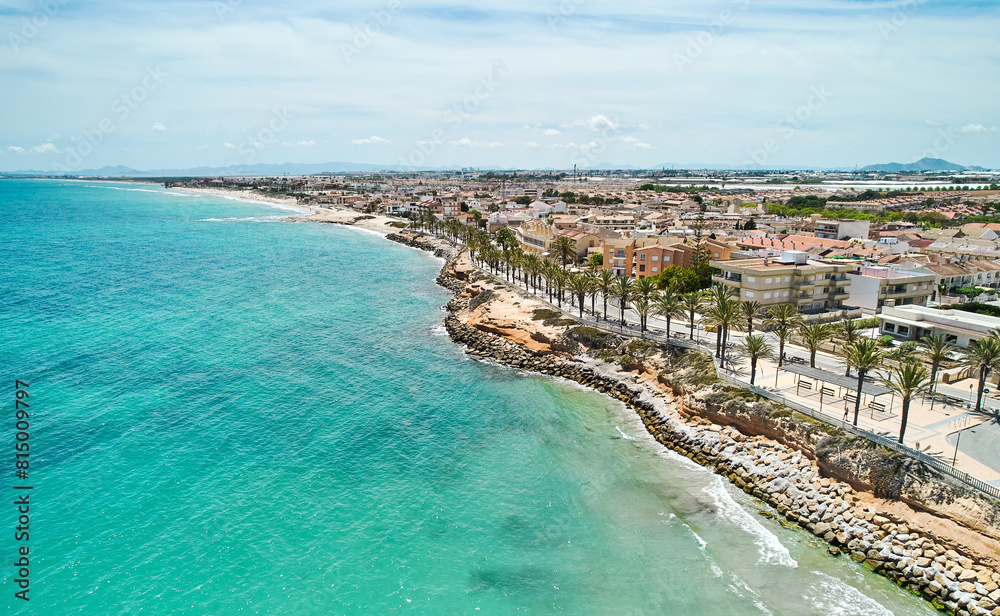 Naklejka premium Aerial shot, drone point of view panoramic image of Torre de la Horadada townscape with sandy beach, turquoise bay and city rooftops at sunny summer day. Costa Blanca, Alicante, Spain