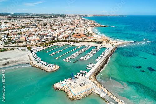Aerial shot, drone point of view panoramic image of Torre de la Horadada townscape with sandy beach, turquoise bay waters and harbor with vessels at sunny summer day. Costa Blanca, Alicante, Spain © Alex Tihonov