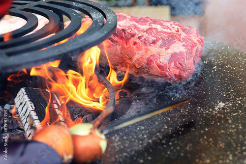 A large pieces of raw fresh steak are grilling on flaming grill. © Silviu
