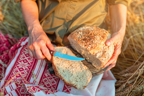 A woman cuts handmade bread on an embroidered towel in a field