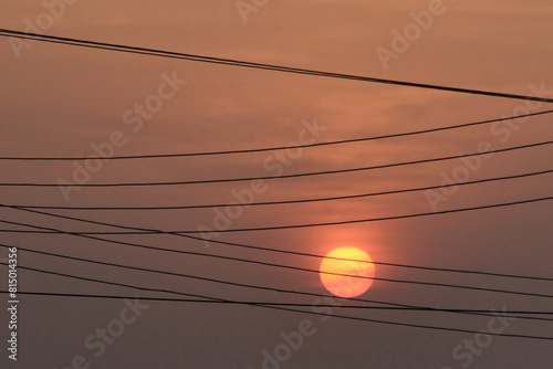Close up view of low setting full round sun with electricity and telephone cable wires in silhouette, Accra, Ghana