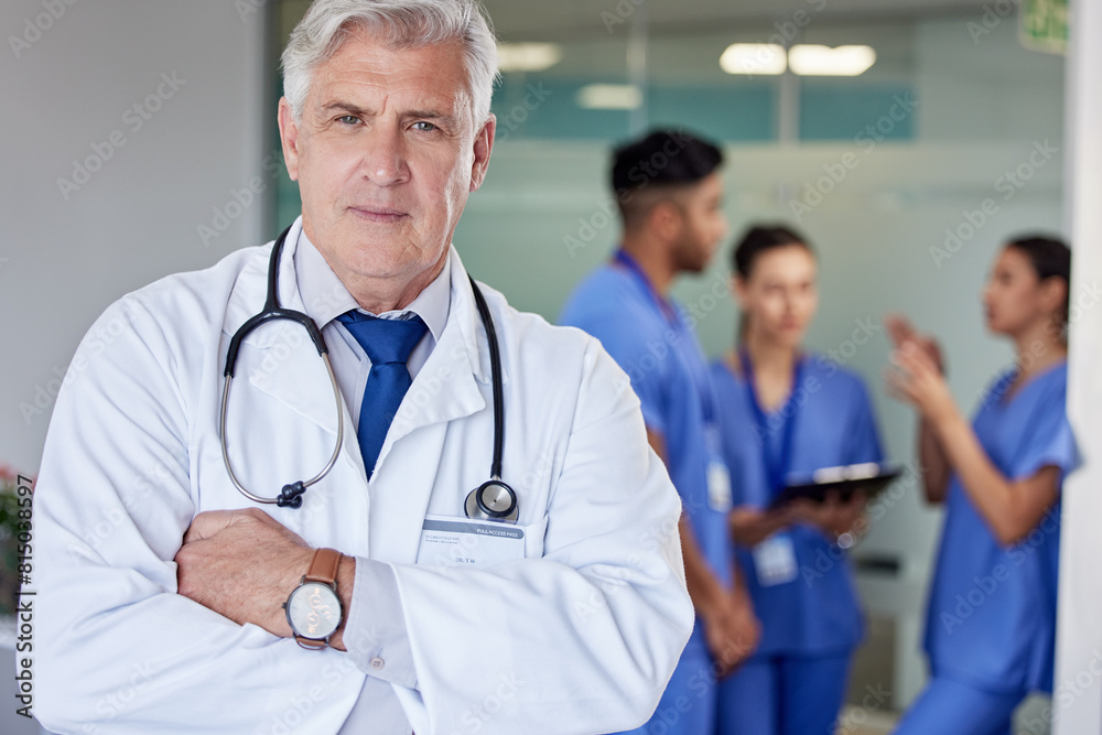 Fototapeta premium Mature doctor, man and arms crossed in portrait at hospital with confidence, team and healthcare services. Senior medic, expert or specialist with pride for professional career with staff in clinic