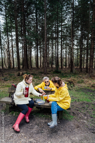 Halt for snack during hiking. Company hikers enjoying picnic on bench, drinking hot tea, eating sandwiches in forest. Friends relaxing and having snack picnic on nature background. Backpacker trip.