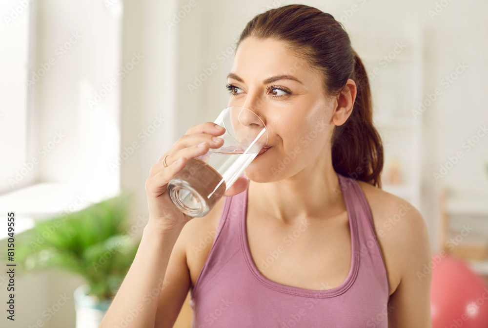 Close up portrait of a young sporty happy woman standing at home after working out drinking a water, looking cheerful and smiling. Sport, fit, healthy nutrition and lifestyle concept. Close up portrait of a young sporty happy woman standing at home after working out drinking a water, looking cheerful and smiling. Sport, fit, healthy nutrition and lifestyle concept.