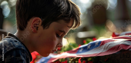 Side view of a praying boy at a tombstone with a gently blurred US flag behind.