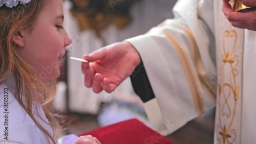 Young Caucasian Catholic Girl in White Alb Festive Outfit Receiving First Holy Communion Sacrament From Catholic Priest