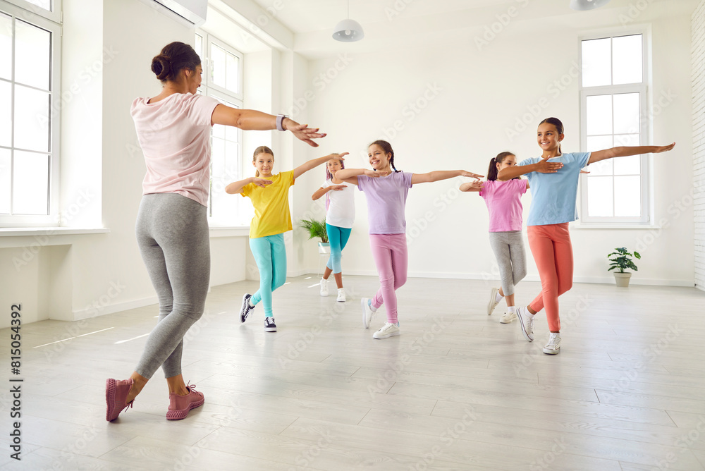 Happy children dancing. Group of little girls in sporty casual clothes are dancing in choreography class. Preteen girls rehearse dance moves with their female coach at children's dance studio. Happy children dancing. Group of little girls in sporty casual clothes are dancing in choreography class. Preteen girls rehearse dance moves with their female coach at children's dance studio.