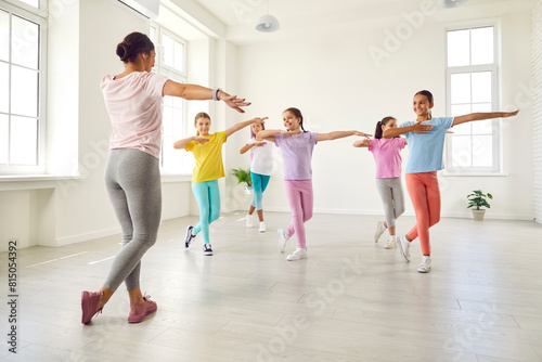 Happy children dancing. Group of little girls in sporty casual clothes are dancing in choreography class. Preteen girls rehearse dance moves with their female coach at children's dance studio.