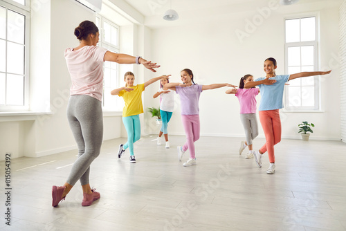 Happy children dancing. Group of little girls in sporty casual clothes are dancing in choreography class. Preteen girls rehearse dance moves with their female coach at children's dance studio.