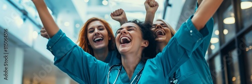 A group of medical professionals in blue scrubs joyfully celebrate success with raised arms and cheers in a hospital hallway photo