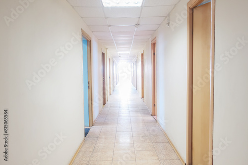 Empty corridor in a hospital with open doors to the rooms and a bright light at the end of the corridor