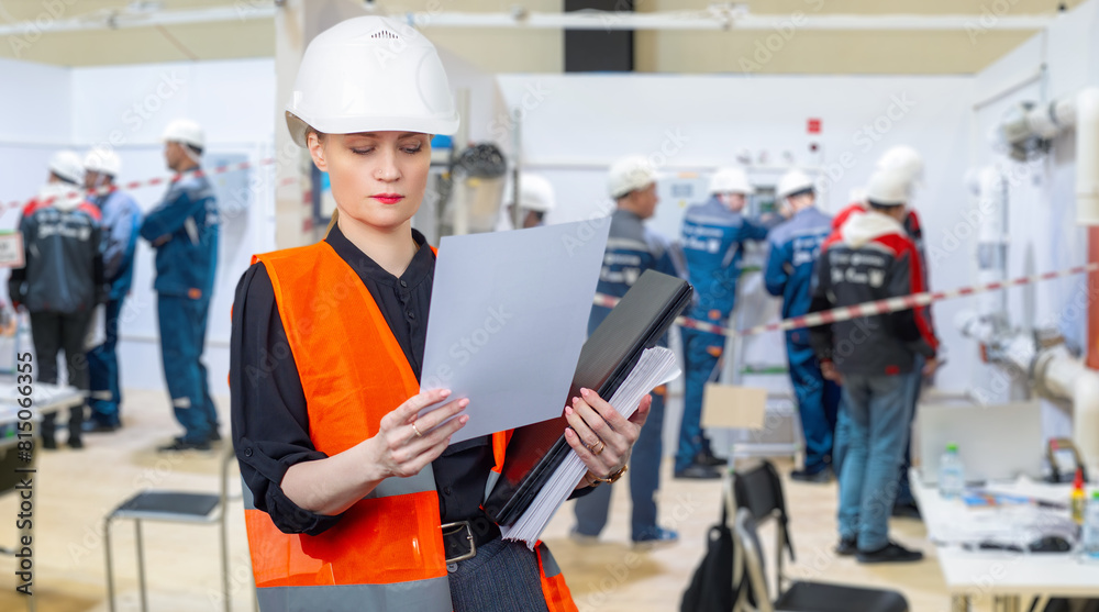 Factory inspector. Girl inspects industrial enterprise. Inspector in vest and helmet. Industrial workers in building. Woman manufactory manager. Inspector reads factory documentation. Art focus Factory inspector. Girl inspects industrial enterprise. Inspector in vest and helmet. Industrial workers in building. Woman manufactory manager. Inspector reads factory documentation. Art focus