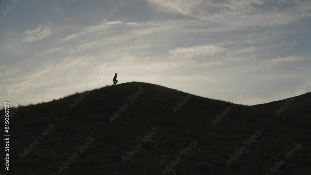 Silhouette of a man running towards the top of a hill against the sky. A man in a suit masters the top. Silhouette of a man running towards the top of a hill against the sky. A man in a suit masters the top.