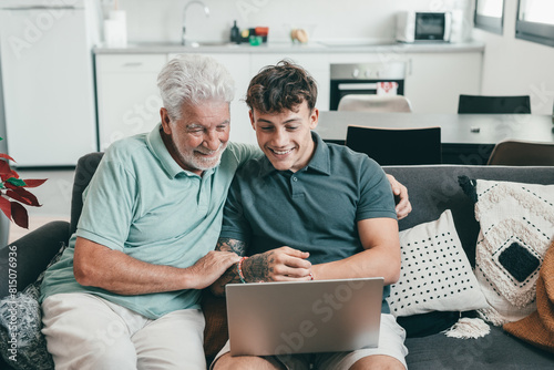Happy family, grandfather learning new computer technology from experienced young grandson, handsome smiling boy teaching how to use computer, how to make online shopping, book travel and vacation