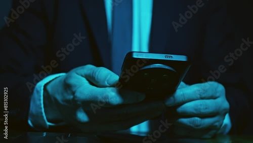 Hands of man in business suit using mobile phone in the dark sitting at table. Dark blue composition scheme