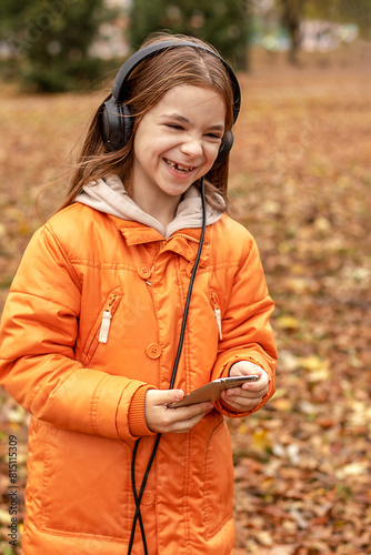Laughing cheerful girl listens to music on headphones in an autumn park.