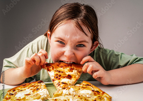 A pre-teenage girl eats a slice of pizza. A hungry little girl in a green t-shirt greedily takes a bite of a large pizza. Close-up  chosen focus.