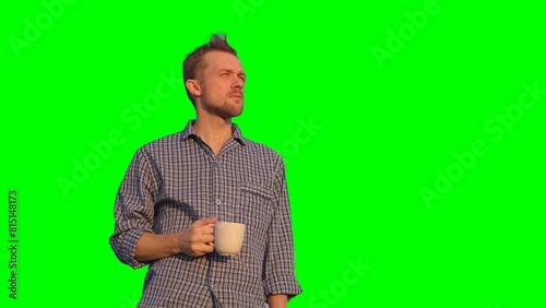 Bearded caucasian male standing outdoor in pajamas looking straight, drinking coffee or tea. Relaxing morning or chillout concept. Clear blue sky at background. High quality 4k footage