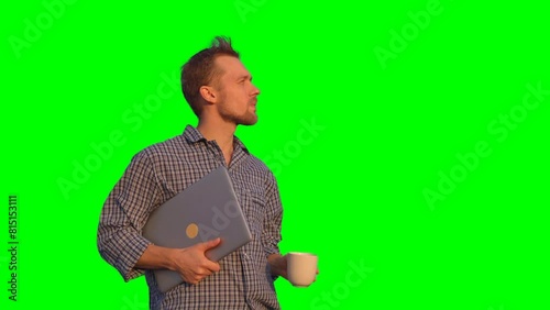 Cheerful bearded caucasian male standing outdoor in pyjamas looking forward, drinking coffee or tea holding laptop. Relaxing morning or chilling concept. High quality green screen