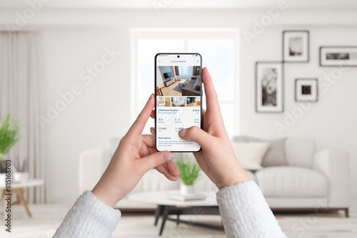 Woman's hands hold a smartphone in a living room interior. Using a luxury homes app to search for rent, blending modern technology with sophisticated living