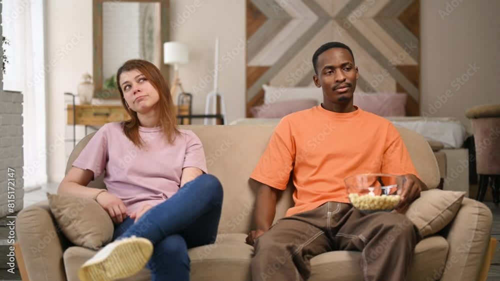 A young couple, a black man and a white woman are sitting next to each other on the sofa and waiting for something A young couple, a black man and a white woman are sitting next to each other on the sofa and waiting for something