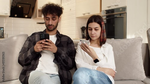 Young couple sitting on the couch at home with their smartphones and don't pay attention to each other. Concept of difficulties in a couple relationship photo