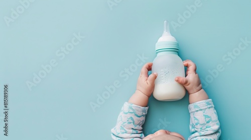 In a heartwarming scene, infant hands tightly grasp a bottle of milk against a light blue floor background. This close-up, pastel-colored image captures the intimacy