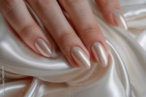 Woman s hand with perfect manicure on a white satin background  in a closeup. Closeup of beautiful female hands and nails in a beige color