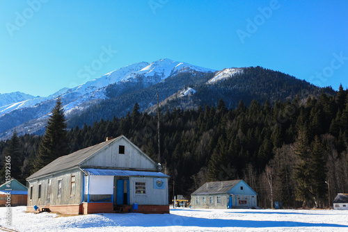 An old wooden house in a mountain valley on a sunny December day. Clear sky, fresh snow, wooden building in a traditional style.