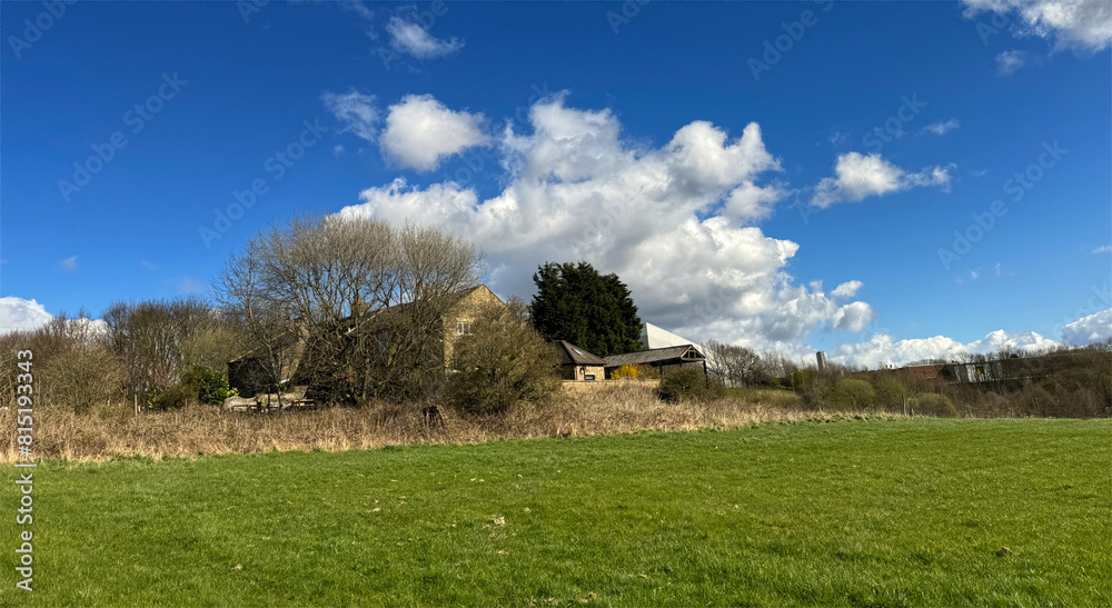 A green meadow leads up to a house partially obscured by trees under a blue sky with clouds, delivering a serene rural landscape near, Bradford, Yorkshire, UK A green meadow leads up to a house partially obscured by trees under a blue sky with clouds, delivering a serene rural landscape near, Bradford, Yorkshire, UK