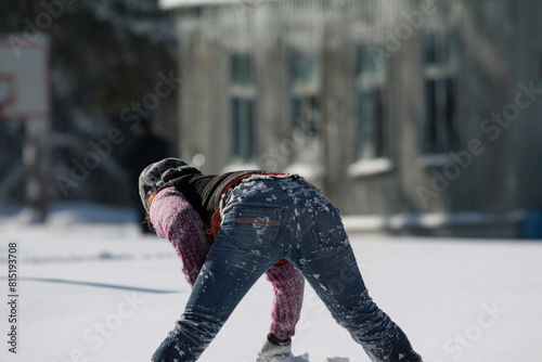 The girl bent down to the ground. Going to play in the snow near the building in the frosty winter