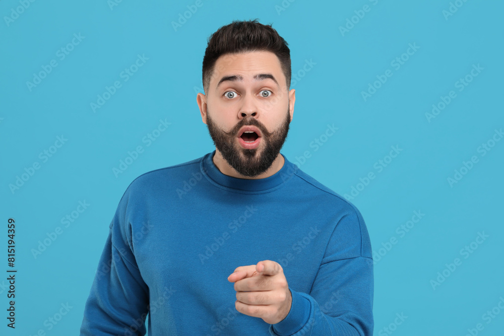 Surprised young man with mustache pointing at something on light blue background Surprised young man with mustache pointing at something on light blue background