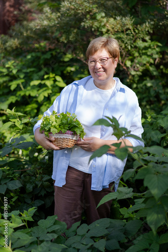 Senior woman stands with a basket of parsley in her garden