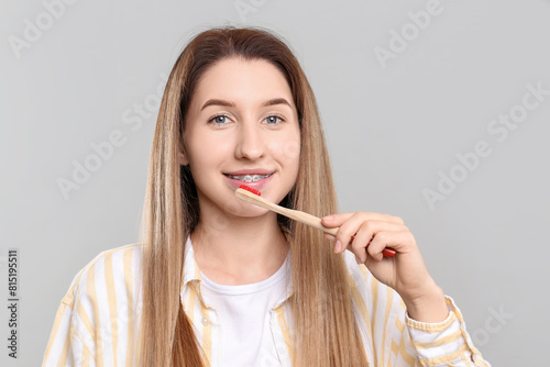 Smiling woman with dental braces cleaning teeth on grey background