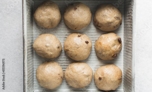 hot cross bun dough rising in a silver baking pan  bun dough rolled into balls in a baking tin  process of making hot cross buns