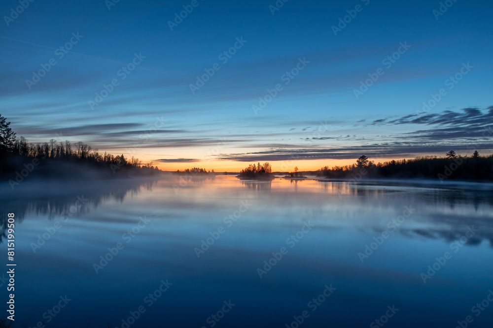 Fototapeta premium Dawn on a northern Minnesota lake near Duluth brings bright colors to the sky as steam rises from the water creating a gentle fog