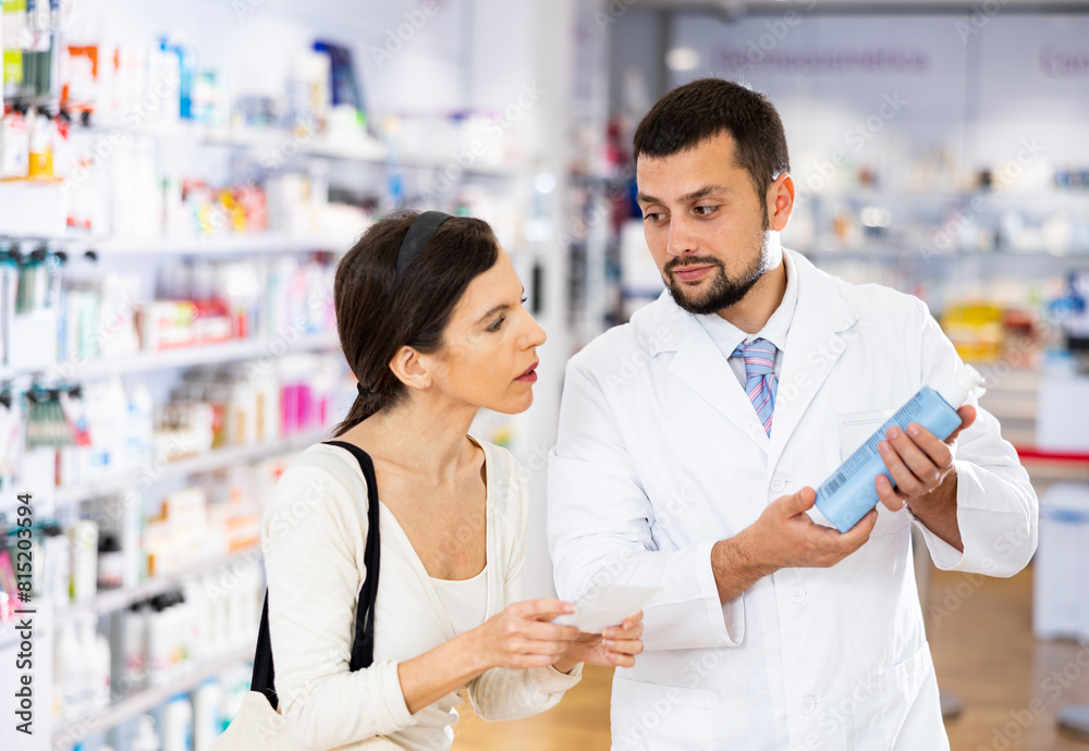 Obraz premium Male pharmacist consulting woman buyer about hair care product in drugstore.
