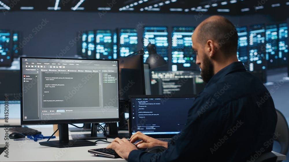 Developer typing code, working in network security data center facility, ensuring optimal performance. IT professional using desktop PC to monitor energy consumption across blade server clusters Developer typing code, working in network security data center facility, ensuring optimal performance. IT professional using desktop PC to monitor energy consumption across blade server clusters
