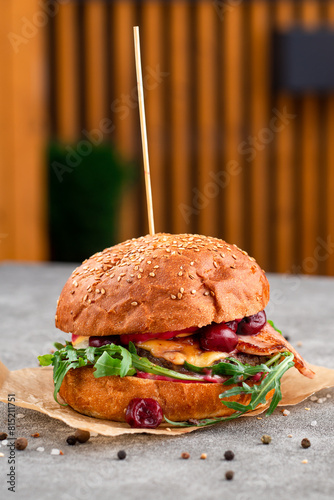 Creative craft burger with fried slices of bacon and cherry, fresh arugula. Street food concept.