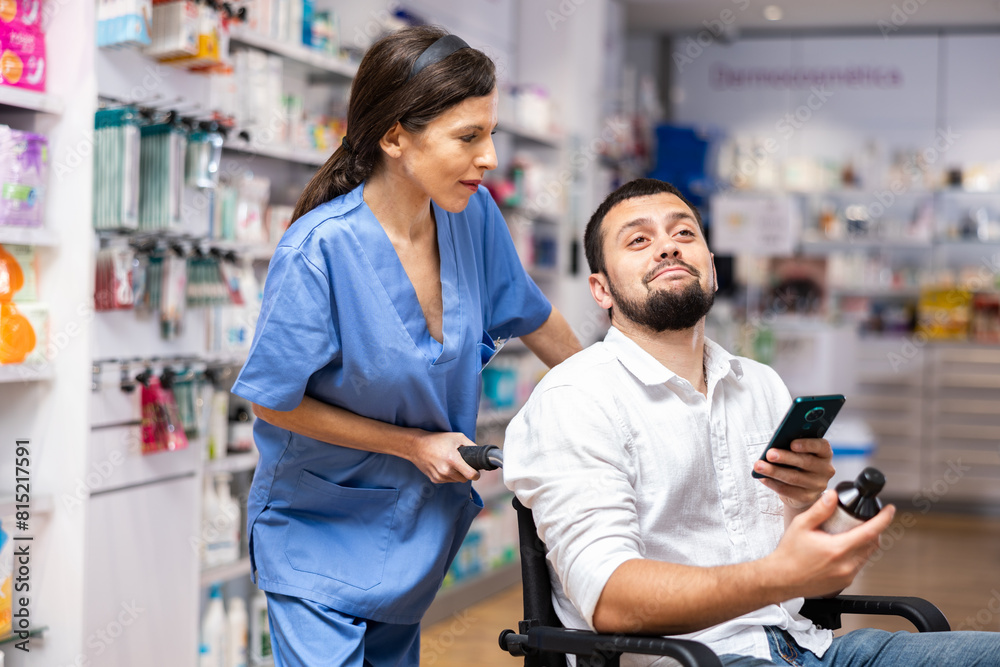 Young adult woman pharmacist consulting disabled man in wheelchair about products at drug store Young adult woman pharmacist consulting disabled man in wheelchair about products at drug store