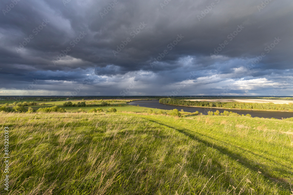 The sky is filled with dramatic storm clouds, creating a striking contrast between the dark sky and the lush greenery below. The sky is filled with dramatic storm clouds, creating a striking contrast between the dark sky and the lush greenery below.