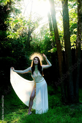 Eine Frau als Göttin steht im Wald im Gegenlicht der Sonne