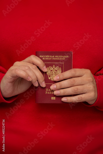 Vertical photo. White woman in red long sleeve sweater holds Russian Federation biometric passport in female hand. Concept of patriotism, tax, loan, travel, tickets, tourism, Russia, trip, control