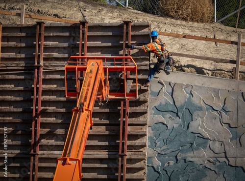 A construction worker standing in a difficult position on a manlift and a retaining wall photo