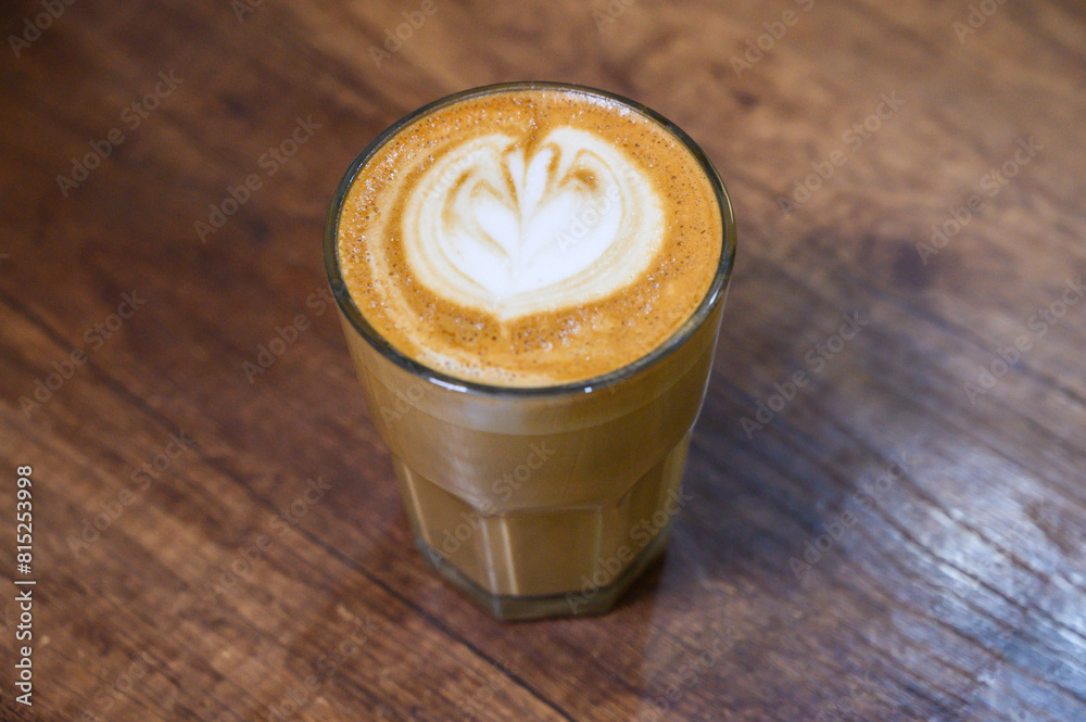 Close-up of a crafted latte with foam art in a glass on a rustic wood surface Close-up of a crafted latte with foam art in a glass on a rustic wood surface