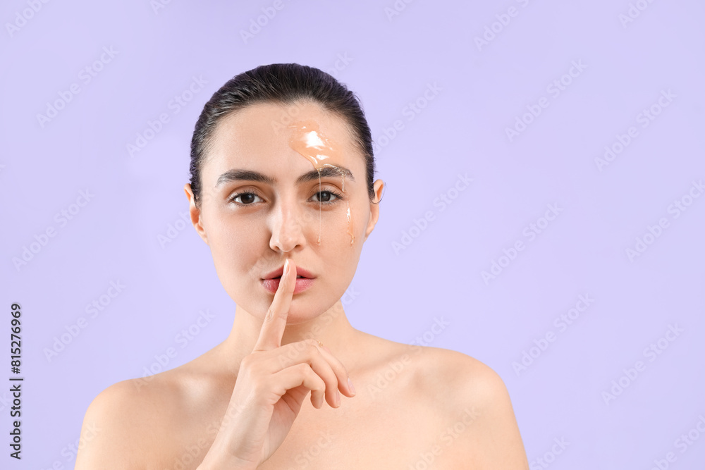 Young woman with dripping honey on her face showing silence gesture against lilac background, closeup Young woman with dripping honey on her face showing silence gesture against lilac background, closeup