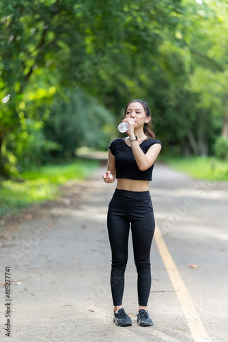 Beautiful young Asian woman in sportswear smiling opens a water bottle to refresh herself before starting a pre-workout preparation. Focus on woman drinking water