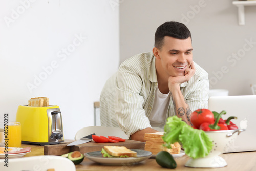 Young man looking for delicious sandwich recipe online in kitchen