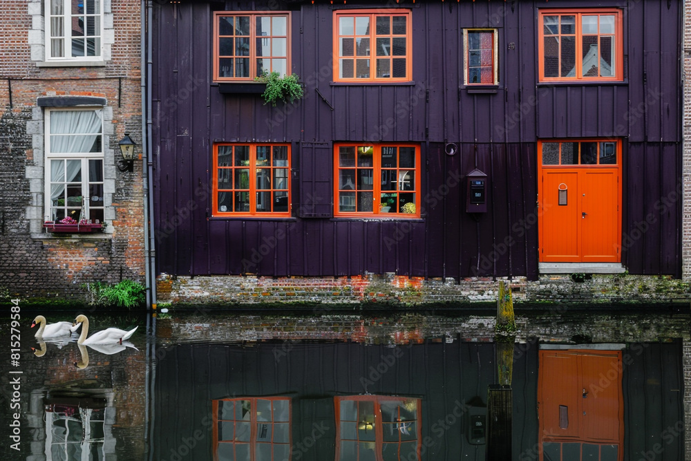 A dark purple house with a bright orange door, located on a serene canal in Bruges, with reflections of medieval buildings and swans gliding by.